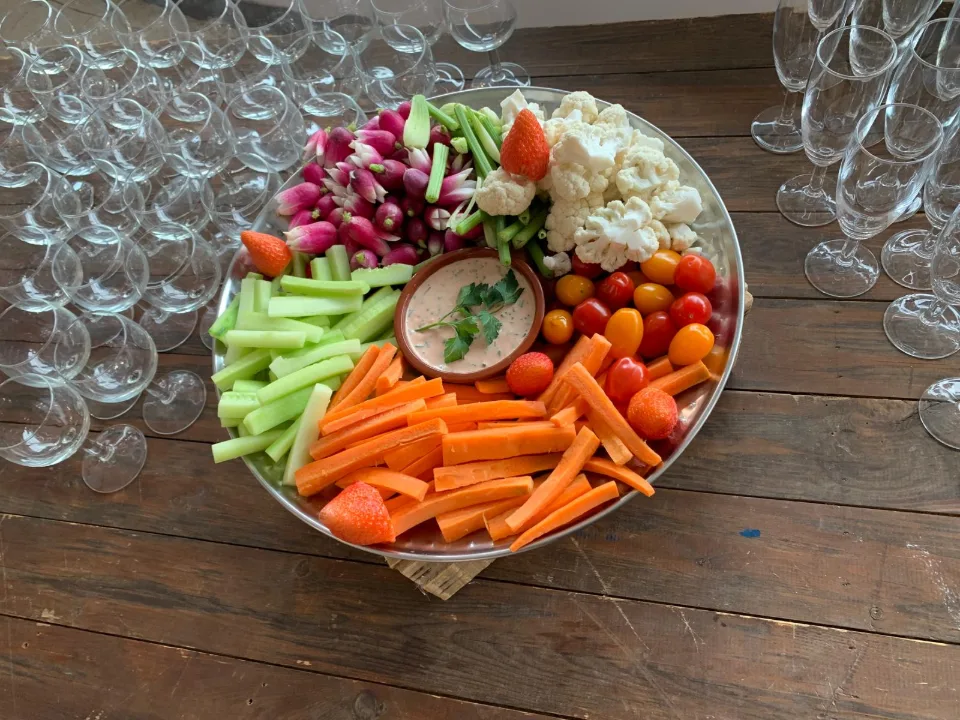Plateau de légumes croquants, tomates cerises et dips sur une table en bois avec des verres en arrière-plan