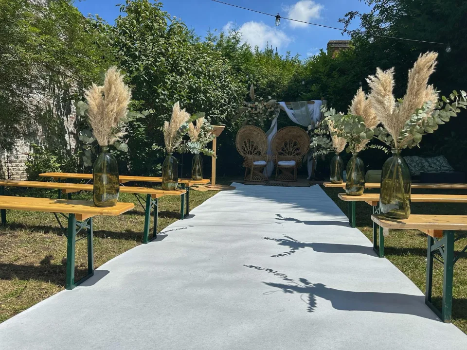 Allée blanche bordée de bancs en bois et de bouquets d'herbes de la pampa menant à la cérémonie laïque