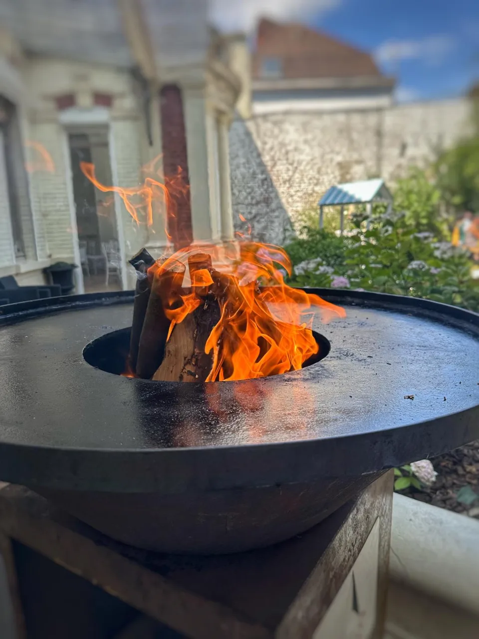 Brasero en fonte avec un feu de bois allumé, installé en terrasse devant la maison