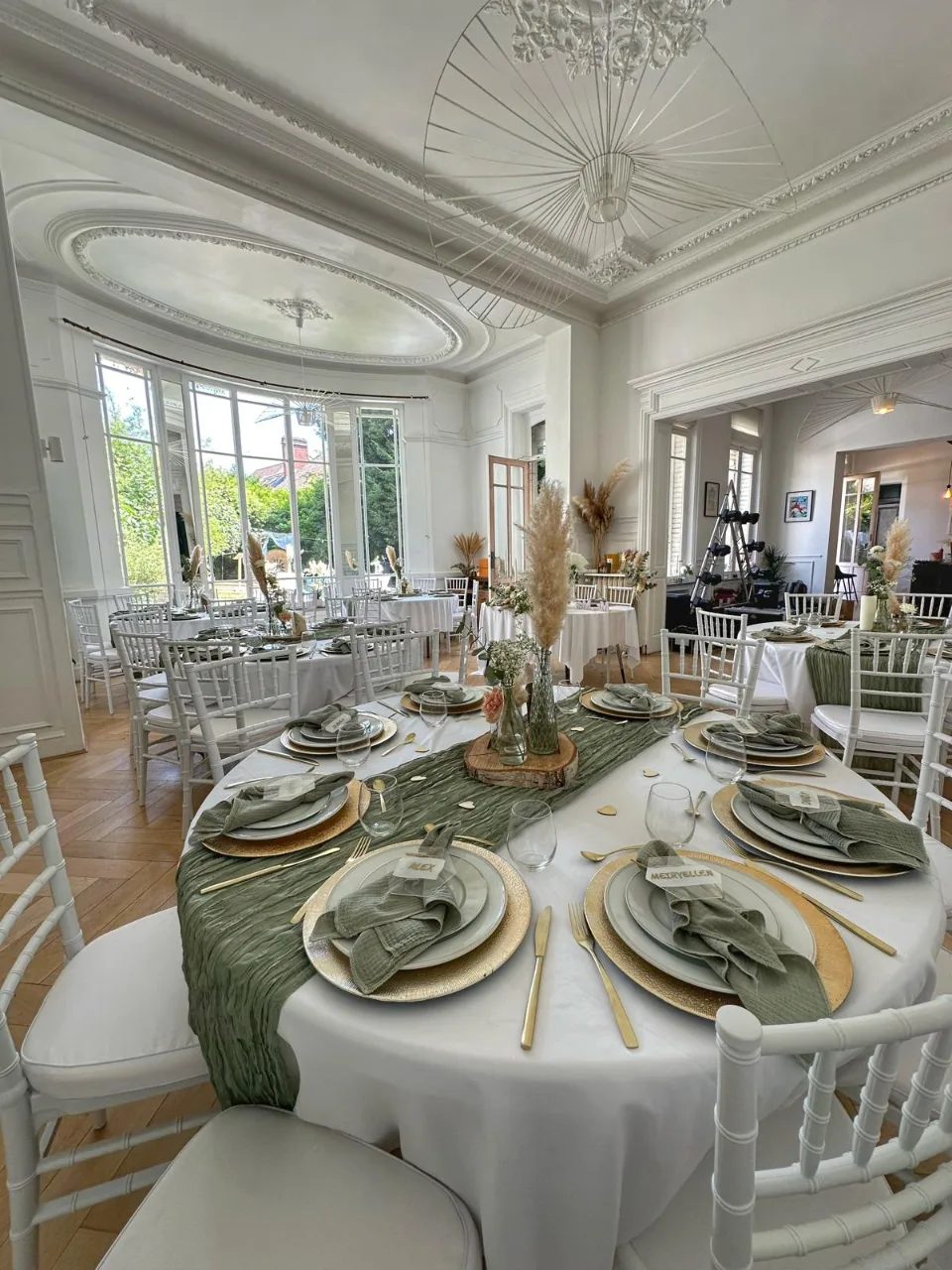 Tables rondes habillées de vert sauge et de fleurs séchées dans la grande salle de réception