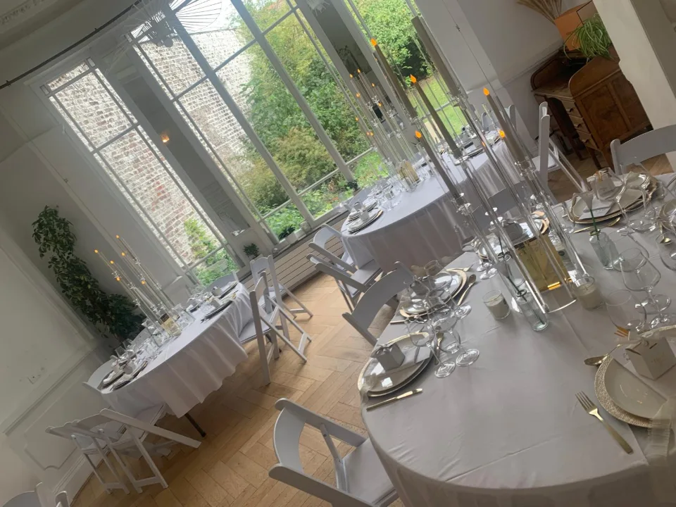 Tables rondes nappées de blanc et dressées près de grandes fenêtres donnant sur le jardin