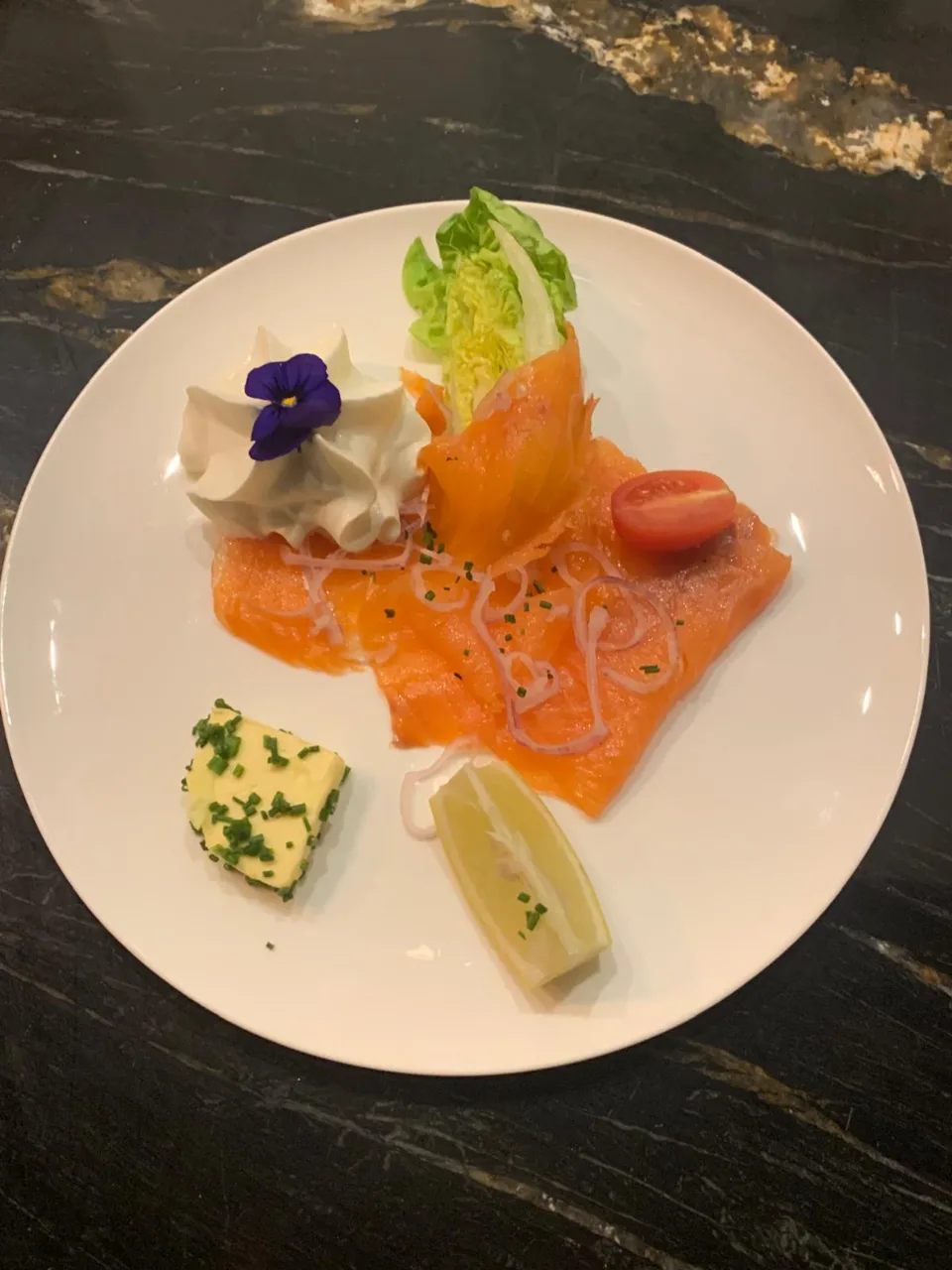 Saumon fumé servi avec crème, beurre persillé, citron, tomate cerise et fleur comestible