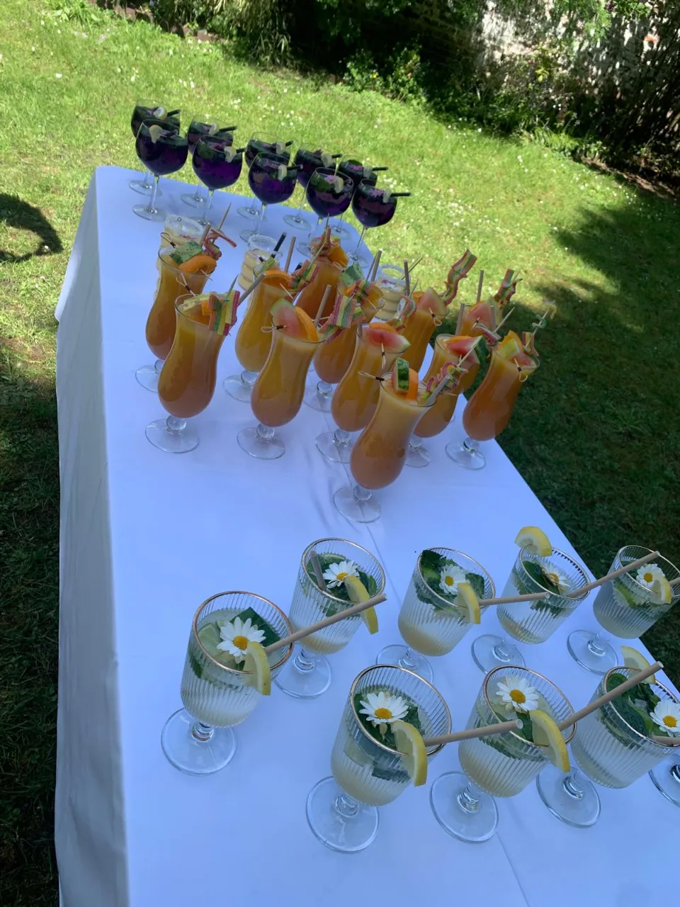 Table dressée dans le jardin avec des cocktails de fruits, des verres givrés à la fleur de pâquerette et des sangrias violettes