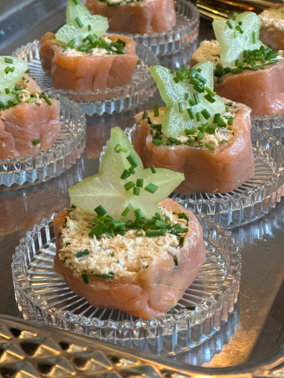 Gros plan sur les bouchées de saumon et fromage frais décorées d'une étoile de concombre, posées sur des coupelles en verre
