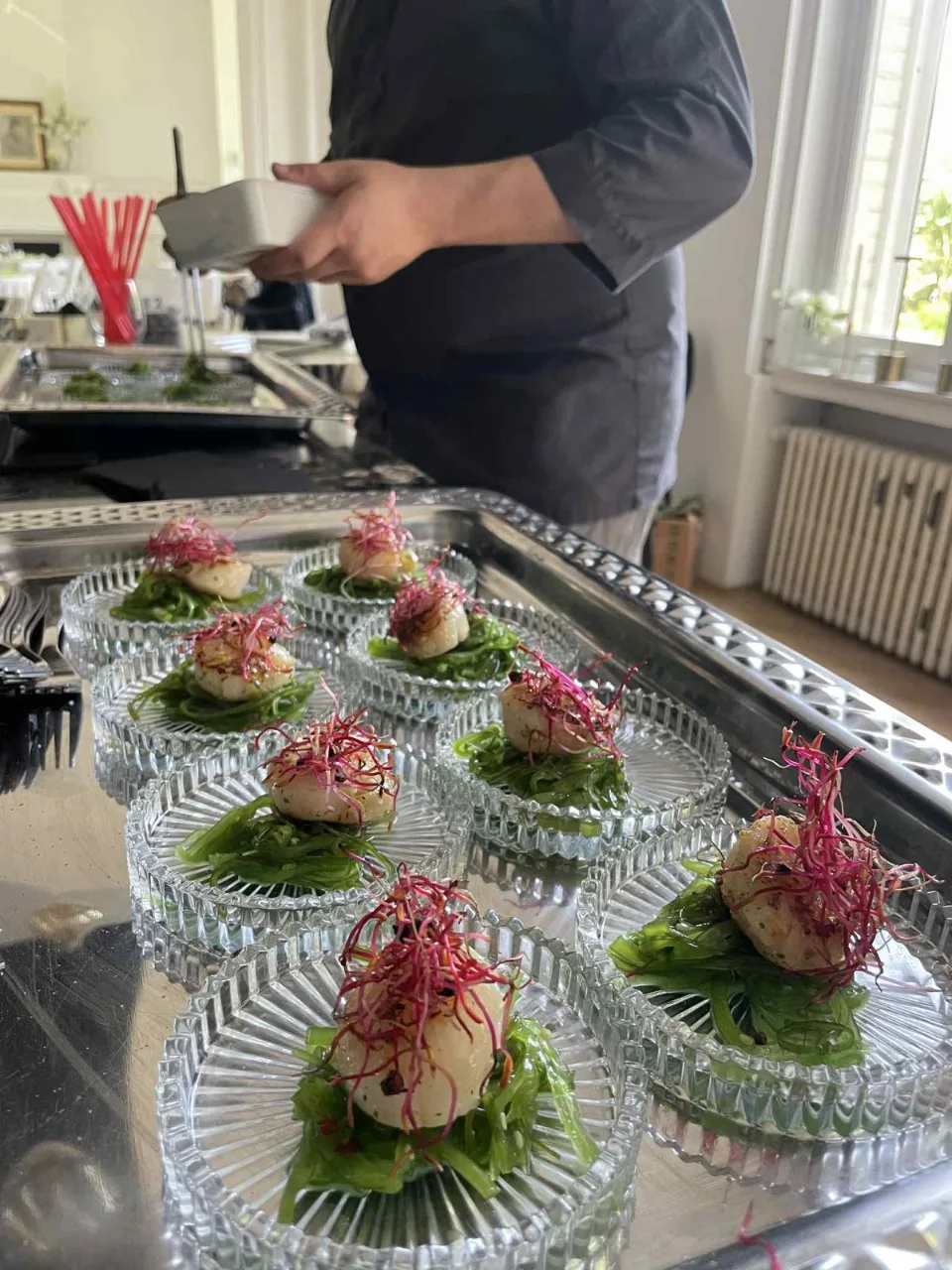 Le chef dresse des coupelles en verre garnies de salade et de Saint-Jacques décorées de pousses roses