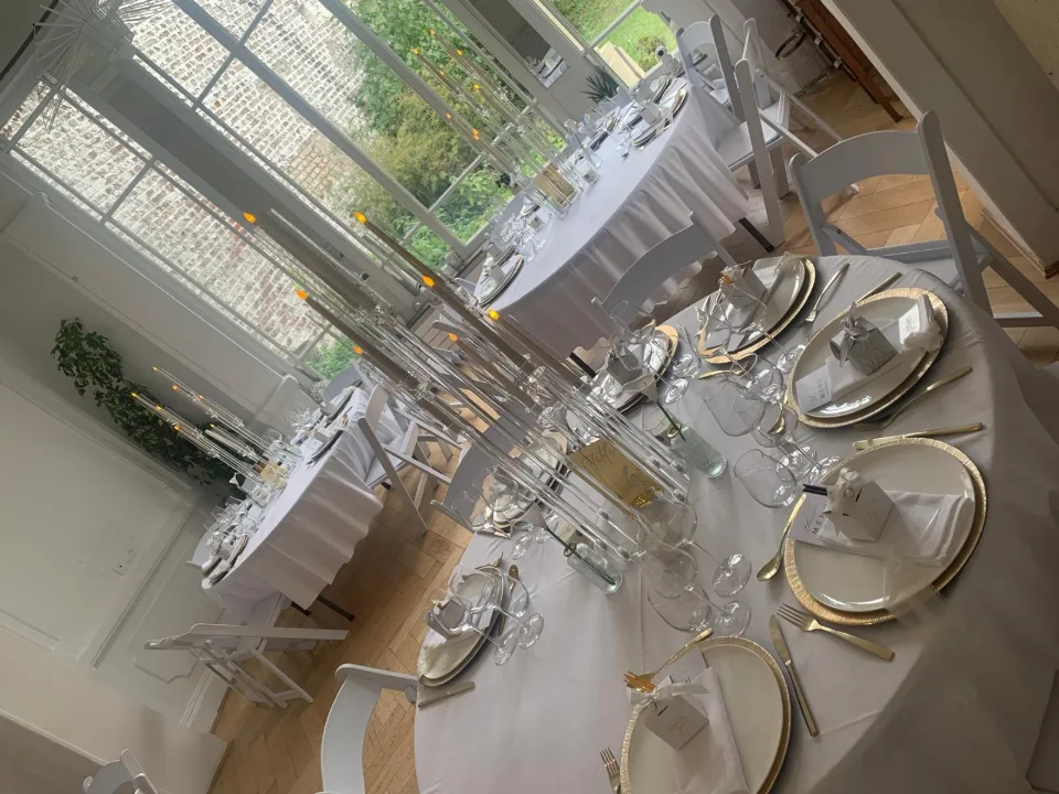 Tables rondes dressées avec assiettes dorées et verres dans la salle de réception lumineuse