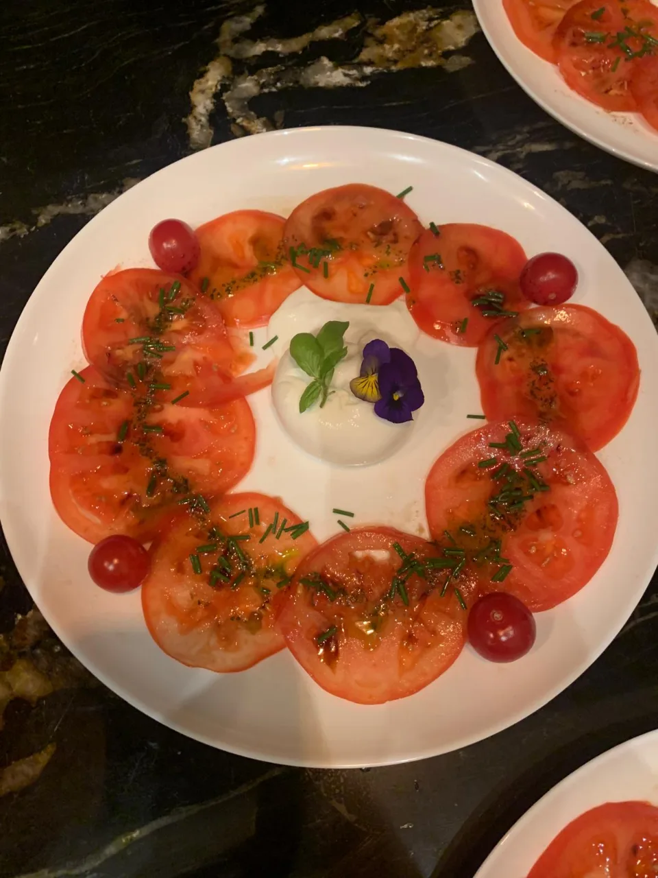Assiette de tomates en rosace avec herbes, tomates cerises et burrata au centre
