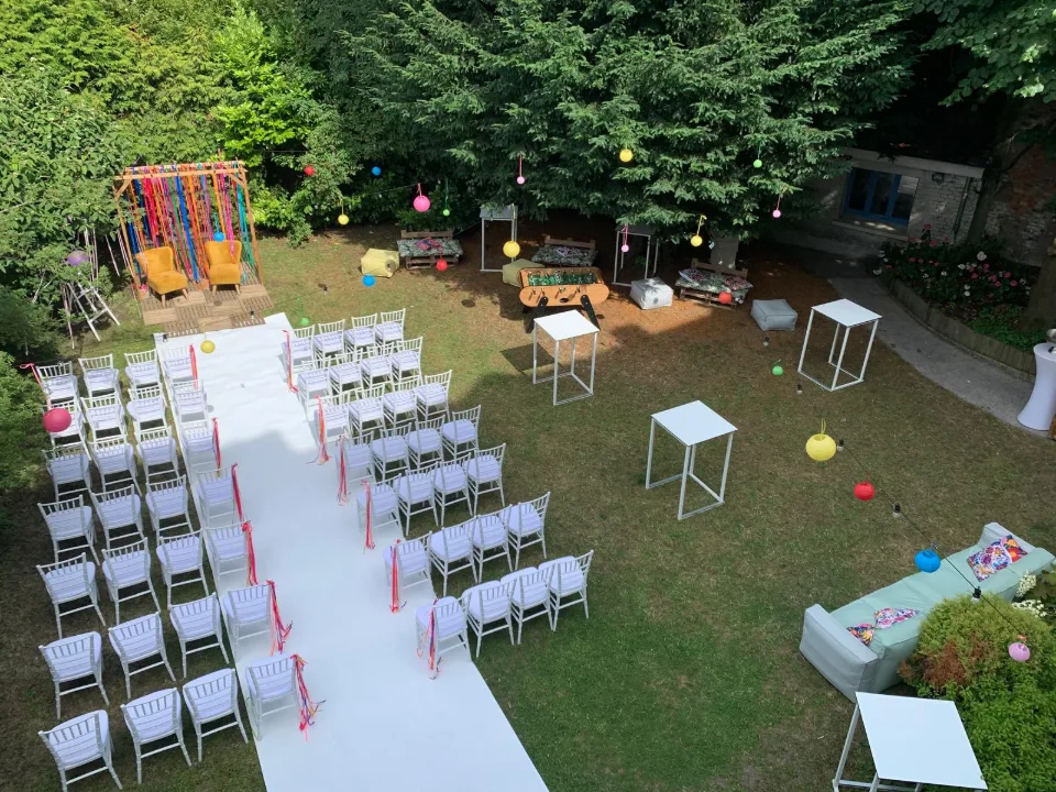 Chaises blanches de part et d'autre d'un tapis blanc, avec lanternes colorées et salon de jardin au fond