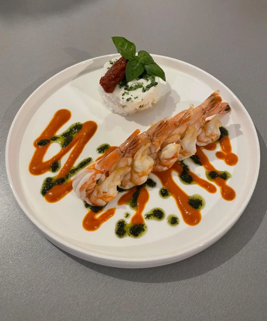 Assiette blanche avec grosses gambas grillées, sauce au poivron, burrata et tomate séchée