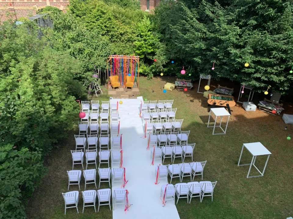 Vue en hauteur du jardin avec rangées de chaises blanches, allée centrale et lanternes colorées