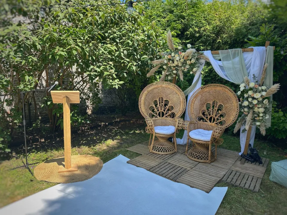 Fauteuils paon, pupitre en bois et tapis blanc installés dans le jardin pour une cérémonie