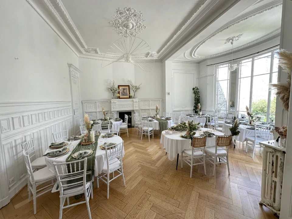 Vaste salon blanc au parquet clair avec tables rondes dressées et chaises blanches