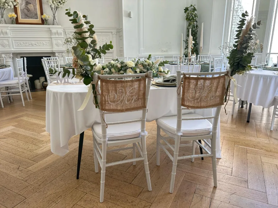 Chaises en bois et cannage ornées de feuillage d'eucalyptus et de fleurs devant la cheminée de la salle