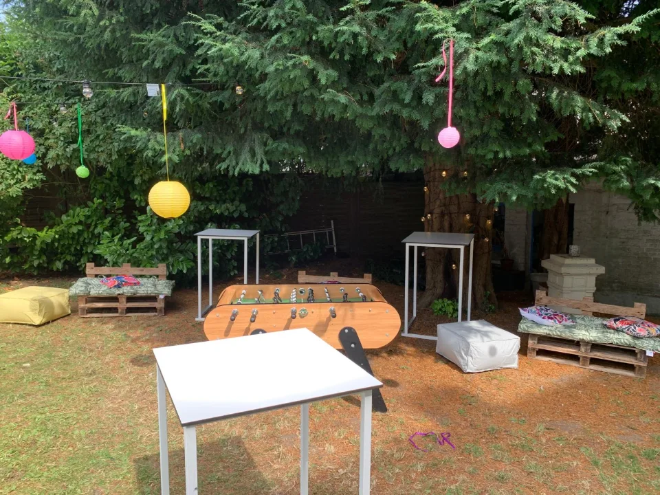 Palettes aménagées en salon, mange-debout blancs et lampions colorés sous les arbres