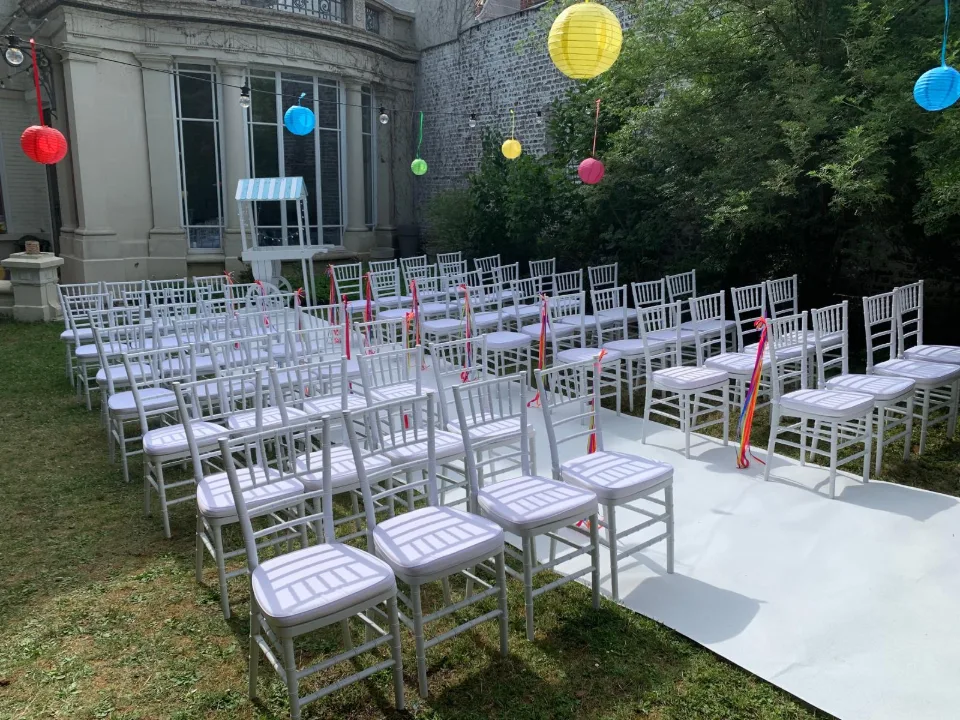 Rangées de chaises blanches et allée de cérémonie sous des lampions colorés
