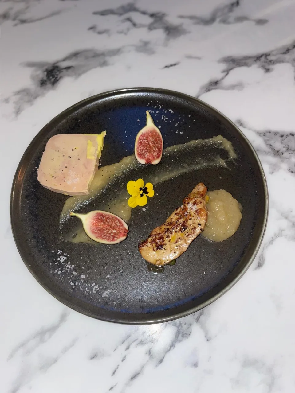 Assiette noire avec foie gras, figues fraîches, magret grillé et fleur jaune comestible